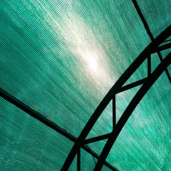 Rete ombreggiante verde installata su struttura in ferro, vista dal basso con luce solare filtrata